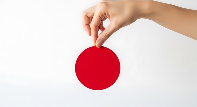 A hand delicately holds a vibrant red circle, isolated on white background, creating a minimalist composition