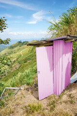 A pink outdoor toilet made of corrugated sheet metal in the mountains.