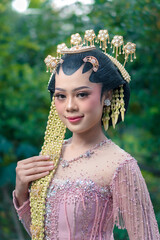 Close-up of an elegant Asian bride wearing a pink Javanese kebaya with intricate beadwork and...