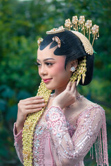 Elegant Asian bride in traditional Javanese kebaya smiling softly, posing gracefully outdoors with...