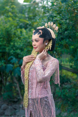 Elegant Asian bride wearing traditional pink Javanese kebaya with intricate embroidery, jasmine...