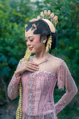 Beautiful Asian bride in Javanese kebaya gently touching her necklace, eyes closed in a serene...