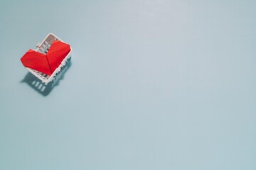 Red origami heart in a white mini basket, top left on light blue background. Perfect for themes of choosing love, valuing relationships, and emotional wellbeing.