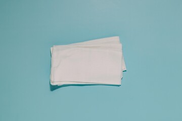 Neat stack of white, folded paper napkins centered on serene blue. Represents cleanliness, hygiene, softness, and everyday essentials for home personal care.