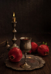 Pomegranates, silver wine goblet and burning candle on wooden table – concept  Rosh Hashanah.