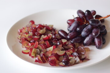 Black seedless grapes and freshly sliced grape pieces on a white plate