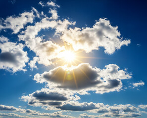 Promienie Słońca na niebieskim niebie przebijające się przez białe obłoki