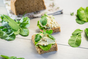 Sandwich with herring paste and greens on a light wooden table