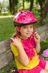 Child in a safety helmet. Portrait of a little cute girl wearing a pink helmet in the park....