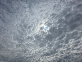 Sun shining through dramatic cloudy sky. The sun faintly glows behind a thick layer of textured,...