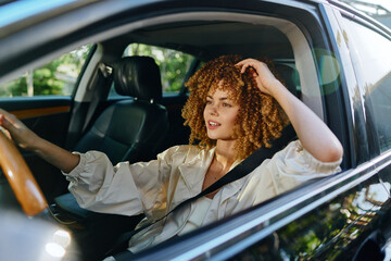 young woman with curly hair driving car during daytime, wearing light blouse and seatbelt, focused...