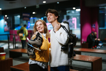 Young couple smiles while holding ice skates in a rink area at night