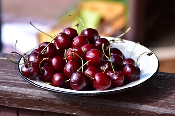 Plate filled with freshly picked ripe cherries on wooden surface. Juicy red fruits glistening in natural light, highlighting summer harvest and organic food.
