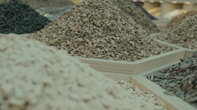 Macro side view of multiple piles of sunflower seeds in a honeycomb arrangement of hexagonal wooden bins. The seeds vary in color and texture, stacked in organized cones across the retail display.