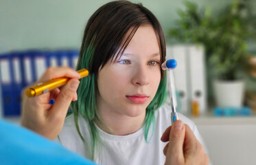 Neurologist shines flashlight and hammer on eyes of teenage patient in clinic close-up. Diagnosis...