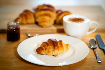 Freshly baked croissant served on a white plate with coffee and jam