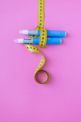 Medical weight loss concept with insulin pens and measuring tape on colorful pink background, symbolizing treatment, diabetes, and obesity control. drugs injection ozempic for weight loss