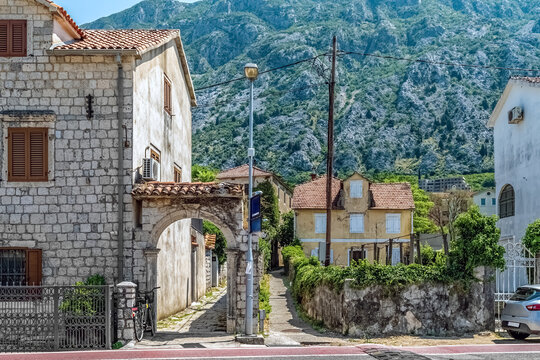 Charming stone houses and an old archway in Kotor, Montenegro, with a stunning backdrop of green mountains. This picturesque view showcases the peaceful residential streets of the historic town