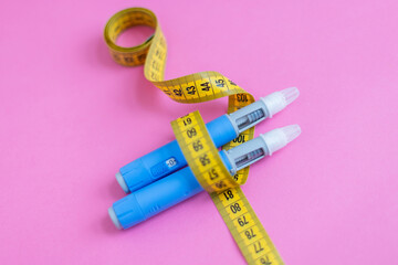 Weight loss and insulin therapy concept. Blue injection pens and yellow measuring tape arranged creatively on pink background. drugs injection ozempic for weight loss