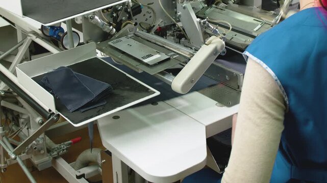 Woman on the specialized sewing machine in factory, dedicated solely to automatic sewing of flaps on blue men's jacket pockets