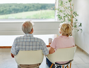 Portrait of a lonely sad, or happy looking outdoors, senior couple looking through window embracing hugging and bonding at home