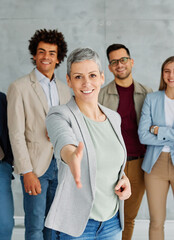 Portrait of a young businesswoman and group of young businesspeople wecoming and offering a...