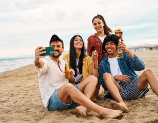 Group of young cheerful people having fun and drinking beer, taking selfie photo with mobile phone camera at the party on the beach looking happy, Enjoying youth and freedom concept