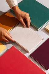 Hand picking a linen-covered book from a flat lay of colorful hardcovers on a textured background.