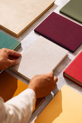 Hand picking a linen-covered book from a flat lay of colorful hardcovers on a textured background.