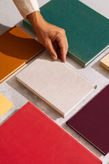 Hand picking a linen-covered book from a flat lay of colorful hardcovers on a textured background.