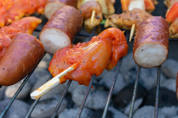 Close-up of grilled sausage and marinated red bell pepper on skewers over charcoal barbecue grill.