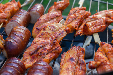 Grilled sausages and marinated chicken fillets sizzling on an open charcoal barbecue at an outdoor cookout.