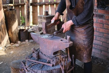 Manual metalworking with a hammer on an anvil in a forge at a medieval crafts festival.