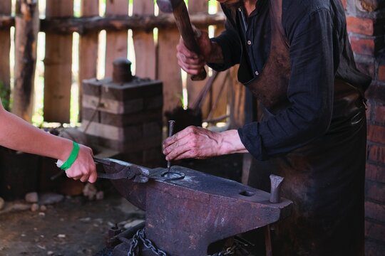Manual metalworking with a hammer on an anvil in a forge at a medieval crafts festival. - Powered by Adobe