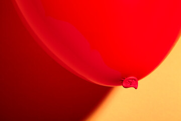Closeup macro studio shot of vibrant dark red balloon against a yellow background with soft shades glowing in sharp contrast shadow