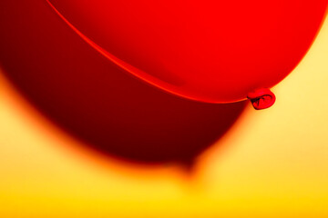 Closeup macro shot of bright dark red balloon against a yellow background with soft shades glowing in sharp contrast shadow