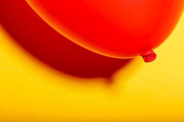Shape and reflective red balloon with shades of redish in the shade on yellow textured wall