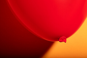 Closeup macro shot of bright dark red balloon against a yellow background with soft shades glowing in sharp contrast shadow