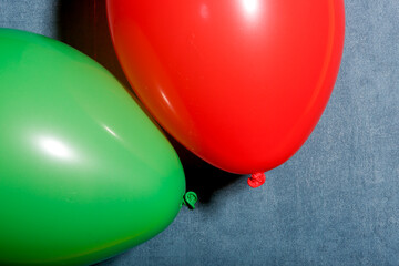 Balloons in primal colours green and red next to each other contrasting against a cold blue paper textured background