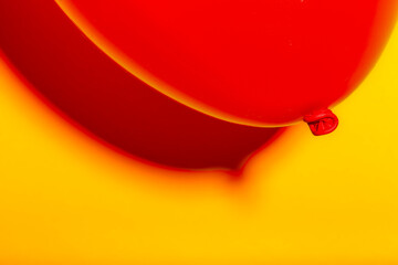 Shape and reflective red balloon with shades of redish in the shade on yellow textured wall