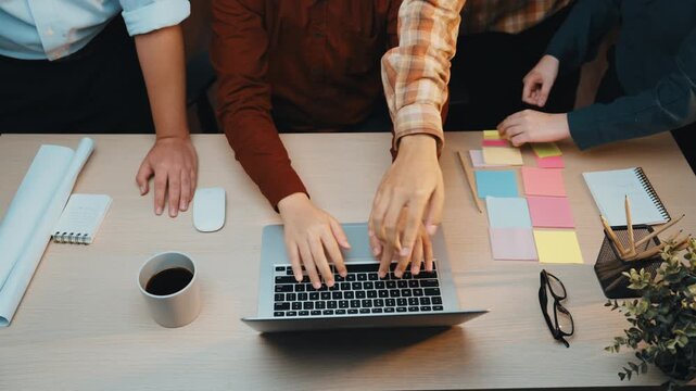 A diverse team collaborates in a modern office setting, interacting around a laptop, with coffee, notebooks, and colorful sticky notes scattered across a wooden desk. SACTR