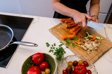 Woman Slicing Carrots and Preparing Vegetables for a Healthy Meal in Modern Kitchen