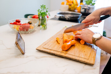 Woman Preparing Carrot Dish in Modern Kitchen with Smartphone and Fresh Ingredients