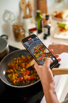 Woman recording cooking video with smartphone saut?ing vegetables in home kitchen