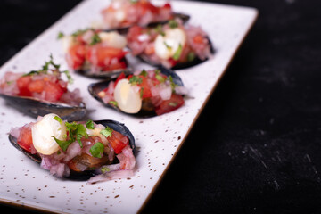 Close-up of the Peruvian coastal appetizer called Choros a la chalaca, served on a white tray against a dark background.