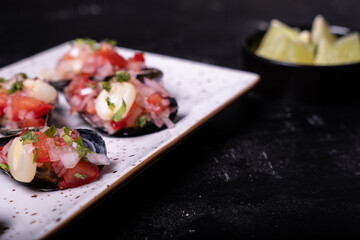 Peruvian appetizer called Choros a la chalaca served on a white platter against a dark background.