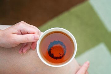 Elegant female hands holding a white porcelain teacup with Chinese black tea, resting on knee for a relaxing daytime tea ritual