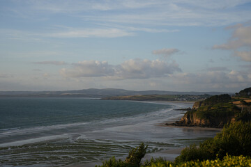 A wide, serene sandy bay on the coast of Brittany, France, during low tide under a soft, hazy sky.
