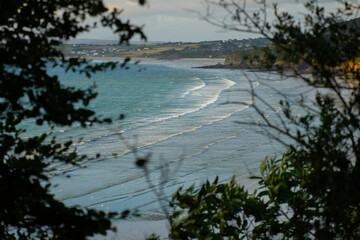 An aerial or high-angle view of a stunning beach in Brittany, France, with turquoise water and white sand creating abstract patterns.