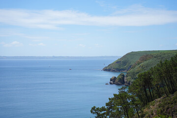 A view of a lush, tree-covered headland extending into the deep blue sea on the coast of Brittany, France.